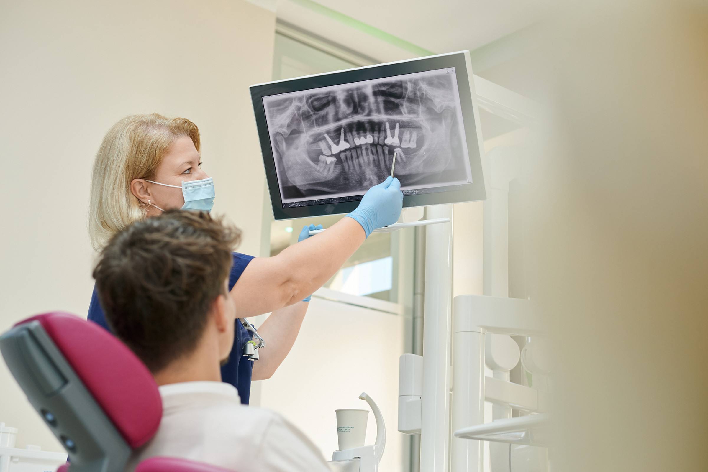 Zahnärztin Stela Xhelili erklärt einem Patienten am Röntgenbild, wie Zahnimplantate geplant werden